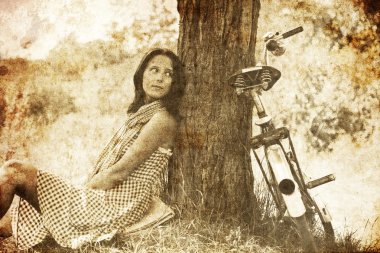 Beautiful girl sitting near bike and tree at rest in forest. Photo in old i clipart