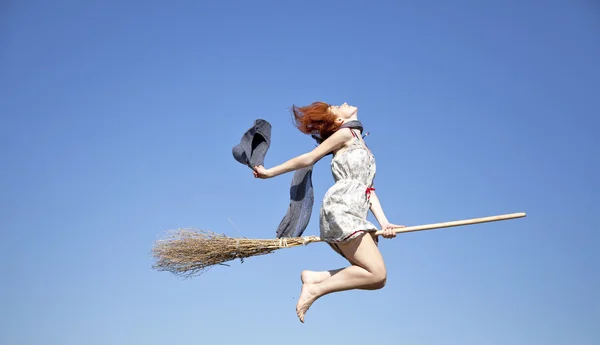 stock image Young red-haired witch on broom flying in the sky