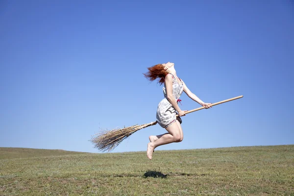 Joven bruja pelirroja en escoba volando sobre campo de hierba verde —  Fotos de Stock