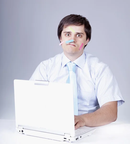 Junger Chef mit weißem Laptop und Notizen im Gesicht. — Stockfoto
