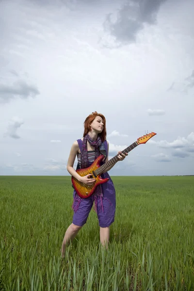 Girl in overalls at green wheat field with guitar. — Stock Photo, Image