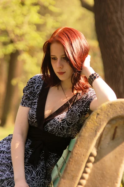 Jonge vrouw zittend op een bankje in een park — Stockfoto