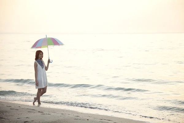 Mooi meisje op het strand bij zonsopgang met paraplu. — Stockfoto