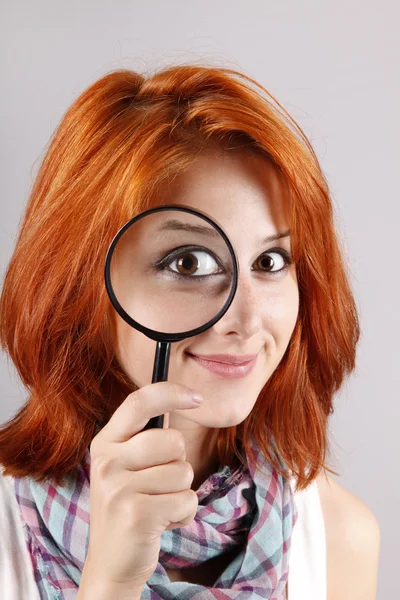 Beautiful red-haired girl with loupe zooming her eye — Stock Photo, Image