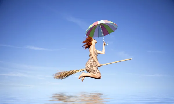 Jovem bruxa ruiva na vassoura voando com guarda-chuva sobre a água — Fotografia de Stock