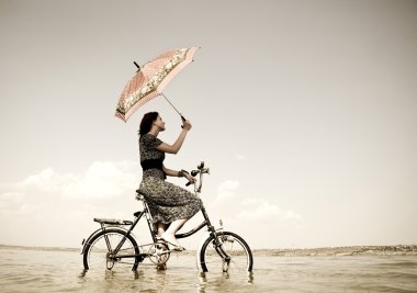 Girl go for a cycle ride at water with umbrella in hand. Photo in retro sty clipart