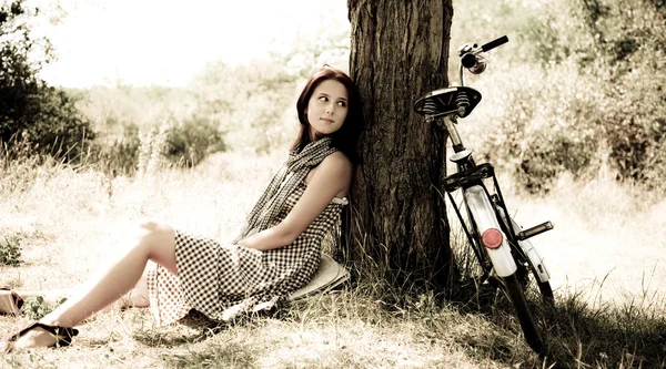 Güzel bir kız bisikleti ve orman içinde kalan ağaca yakın oturuyor. retro fotoğraf — Stok fotoğraf