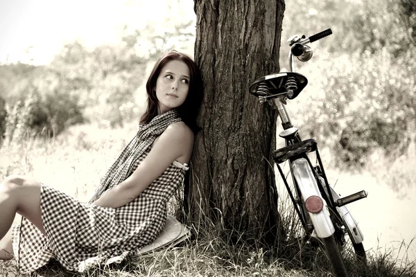 Menina bonita sentado perto de bicicleta e árvore em repouso na floresta. Foto em retro — Fotografia de Stock