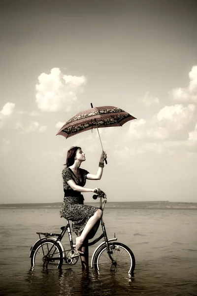 Девушка едет кататься на велосипеде у воды с зонтиком в руке. Фото в стиле ретро — стоковое фото
