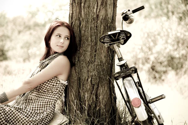 Hermosa chica sentada cerca de la bicicleta y el árbol en reposo en el bosque. Foto en retro —  Fotos de Stock