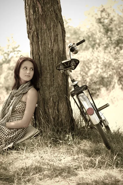Mooi meisje zit in de buurt van fiets en boom in rust in bos. foto in retro — Stockfoto