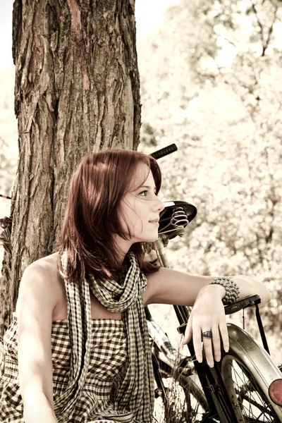 Mooi meisje zit in de buurt van fiets en boom in rust in bos. foto in retro — Stockfoto