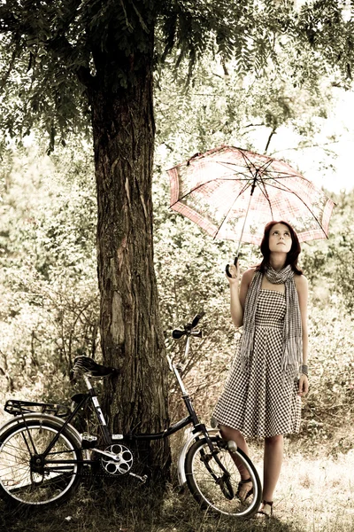 Hermosa chica cerca de bicicleta y árbol en reposo en el bosque. Foto en retro —  Fotos de Stock
