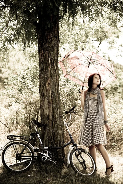 Menina bonita perto de bicicleta e árvore em repouso na floresta. Foto em retro — Fotografia de Stock