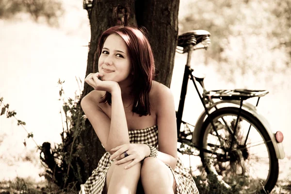 Vacker flicka sitter nära cykel och träd i vila i skogen. Foto i retro — Stockfoto