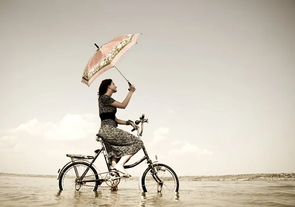 Chica ir a dar un paseo en bicicleta en el agua con paraguas en la mano. Foto en retro sty —  Fotos de Stock