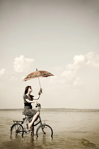 女の子は手に傘と水でサイクル乗るのために行きます。レトロなスタイルの写真 — ストック写真