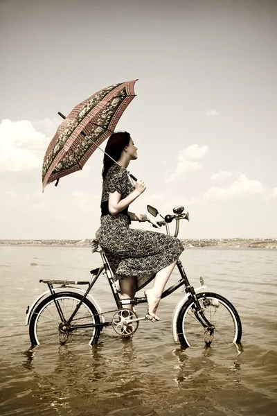 Tjej går för en cykel tur på vattnet med paraply i hand. Foto i retro stil — Stockfoto