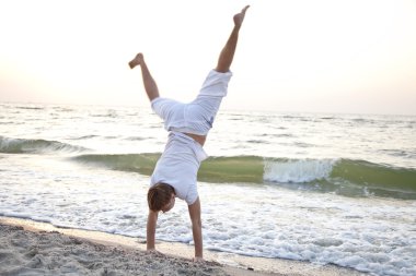 Young man doing cartwheels on the beach clipart