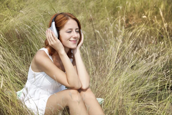 Vacker rödhårig flicka på gräs med hörlurar — Stockfoto