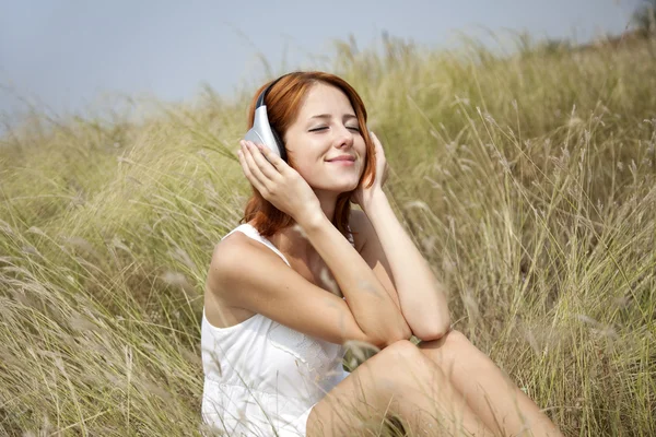Krásná rusovlasá dívka v trávě se sluchátky — Stock fotografie