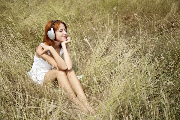 Όμορφη κοκκινομάλλα κοπέλα στη χλόη με ακουστικά — Φωτογραφία Αρχείου