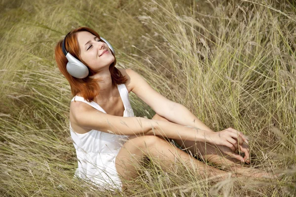 Красива руда дівчина на траві з навушниками — стокове фото