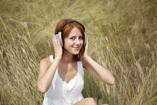Vacker rödhårig flicka på gräs med hörlurar — Stockfoto