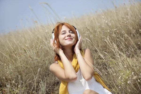 ヘッドフォンで草で美しい赤い髪の少女 — ストック写真