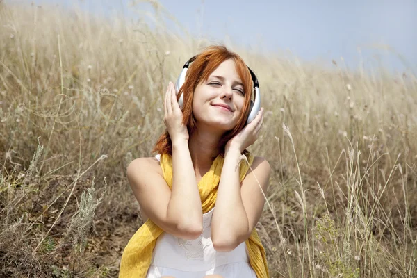 Hermosa chica pelirroja en la hierba con auriculares — Foto de Stock