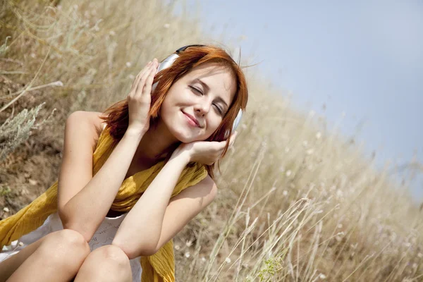 Красива руда дівчина на траві з навушниками — стокове фото
