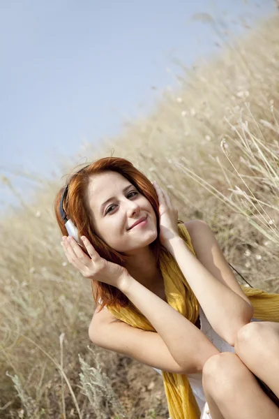 Όμορφη κοκκινομάλλα κοπέλα στη χλόη με ακουστικά — Φωτογραφία Αρχείου