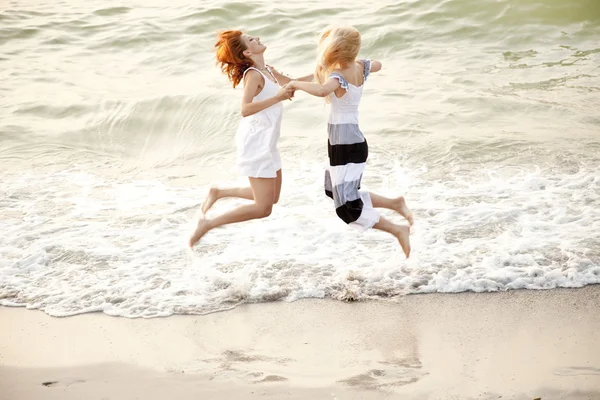 Twee mooie jonge vriendinnen springen op het strand — Stockfoto