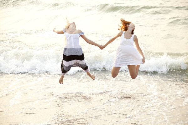 Two beautiful young girlfriends jumping on the beach