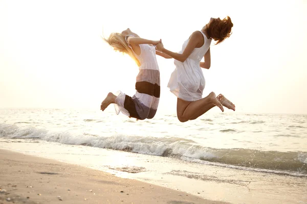 Två vackra unga flickvänner hoppa på stranden — Stockfoto