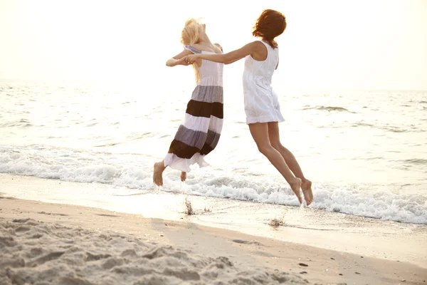 Twee mooie jonge vriendinnen springen op het strand — Stockfoto