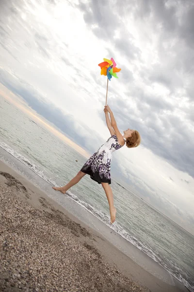 Ragazza bionda che salta con turbina eolica in spiaggia . — Foto Stock