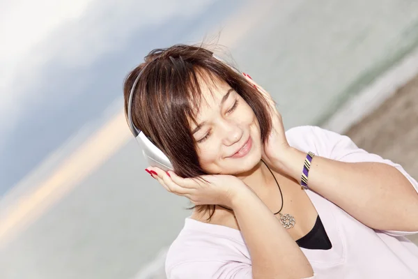 年轻 brunet 女孩戴着耳机在海滩. — 图库照片