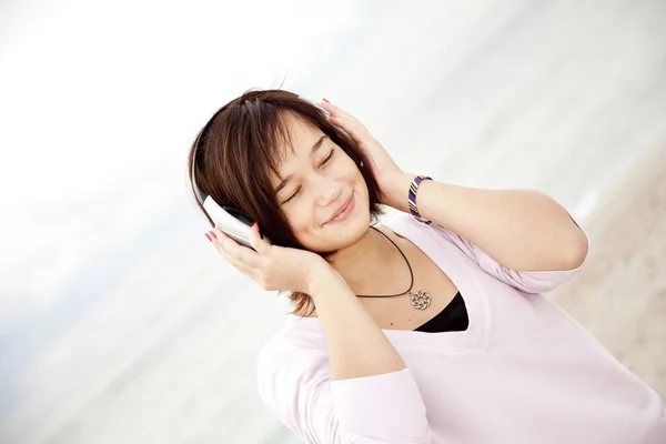 Młoda dziewczyna brunet z słuchawkami na plaży. — Zdjęcie stockowe