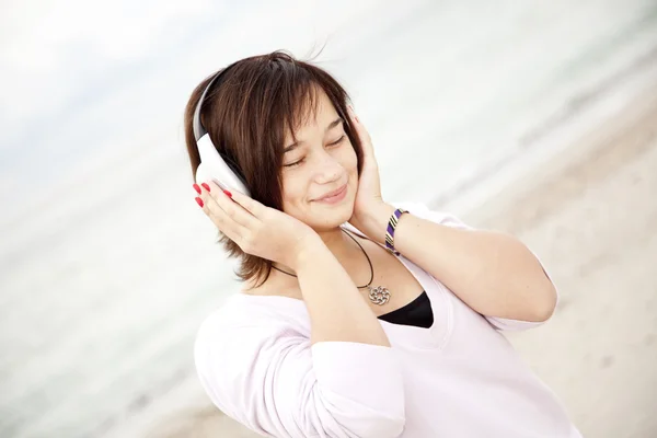 Menina morena jovem com fones de ouvido na praia . — Fotografia de Stock