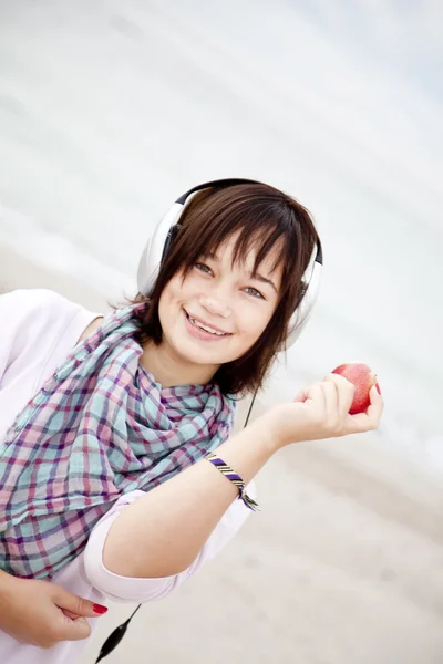 Brunet meisje met hoofdtelefoons en apple op het strand. — Stockfoto