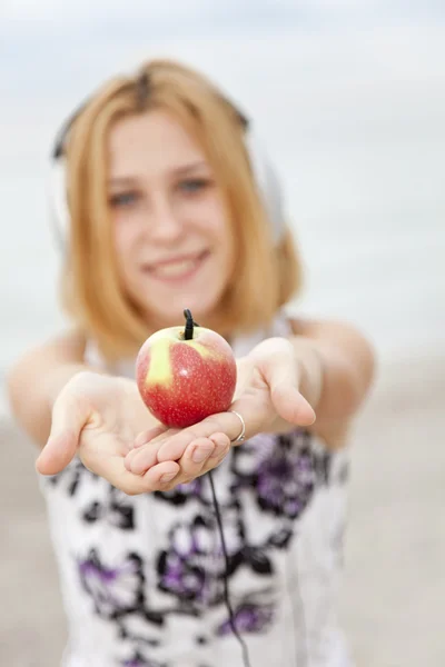 Giovane ragazza bionda con cuffie e mela sulla spiaggia . — Foto Stock