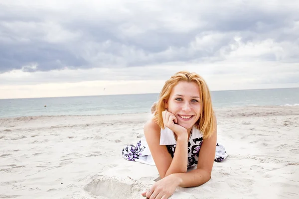 Prachtige blond meisje liggend op het zand op het strand in regenachtige dag. — Stockfoto