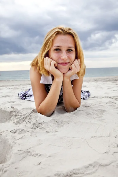 Hermosa chica rubia tumbada en la arena en la playa en días lluviosos . —  Fotos de Stock