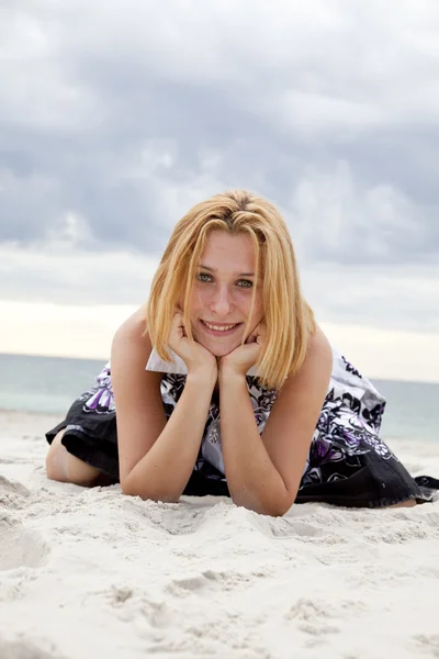 Όμορφη ξανθιά κοπέλα που βρίσκεται στην άμμο στην παραλία στο βροχερές ημέρες. — Φωτογραφία Αρχείου