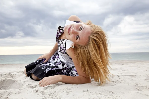 Schönes blondes Mädchen, das an einem regnerischen Tag am Strand auf Sand liegt. — Stockfoto
