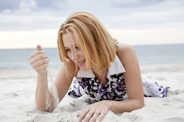 Schönes blondes Mädchen, das an einem regnerischen Tag am Strand auf Sand liegt. — Stockfoto