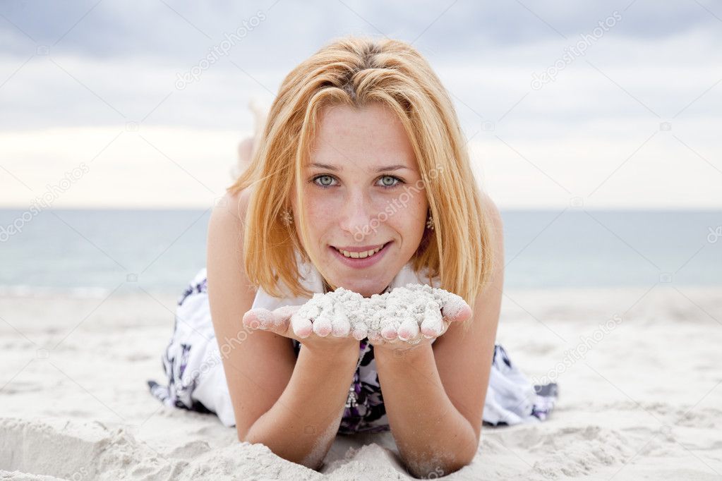 Beautiful blonde girl lying on sand at the beach in rainy day.