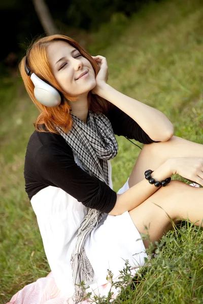 Ung flicka med hörlurar som sitter på grönt gräs — Stockfoto