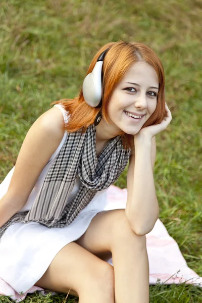Chica de la moda joven con auriculares sentado en la hierba verde —  Fotos de Stock